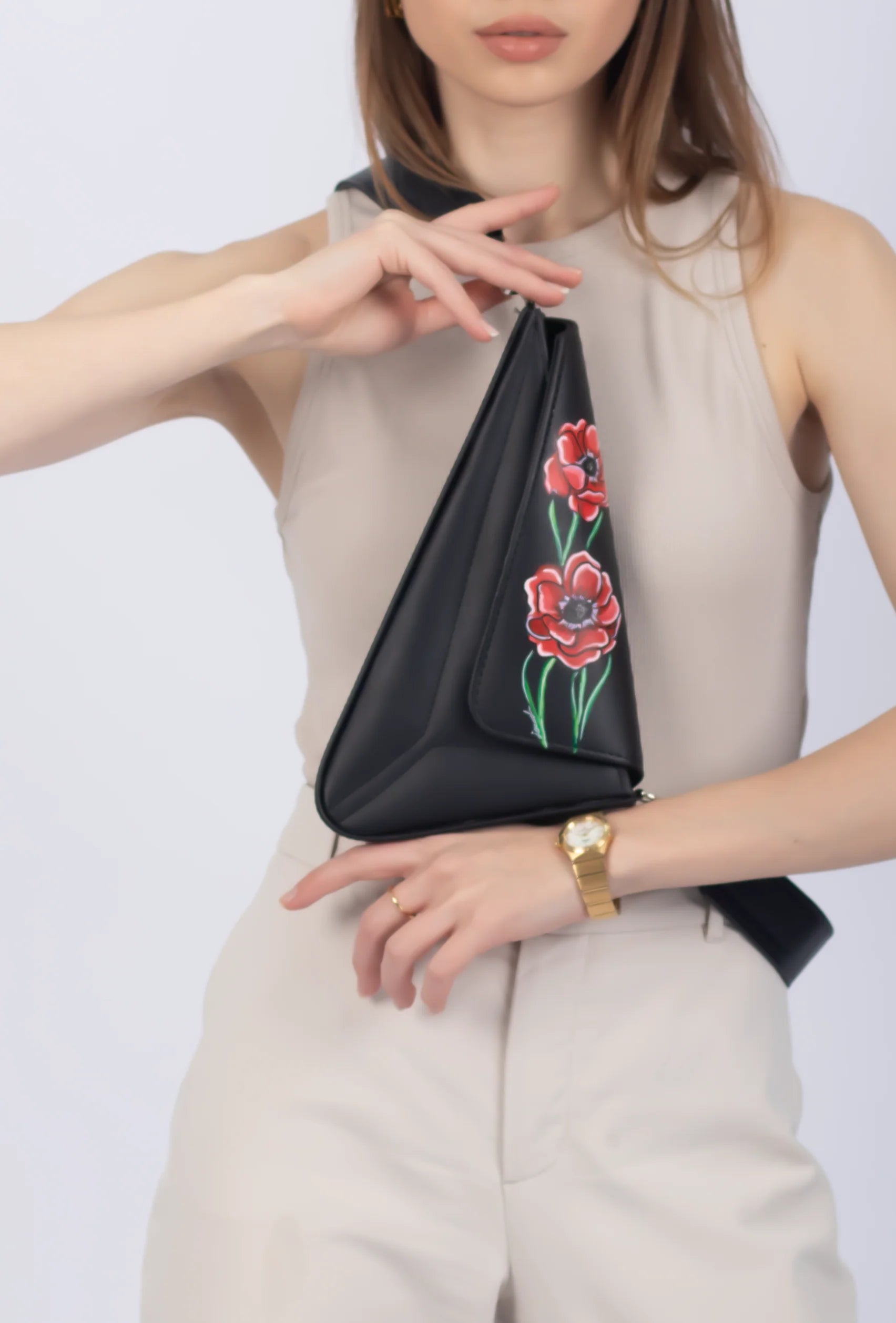 Person holding a black sling bag with floral embroidery on a white background