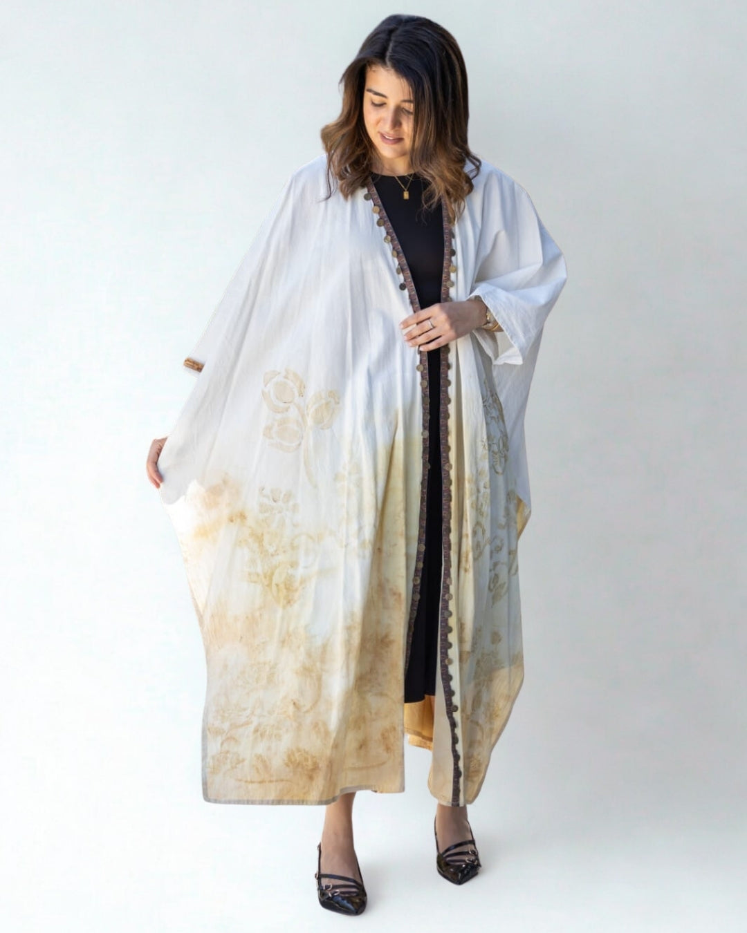 Woman wearing a long, light-colored dress with a floral pattern on a white background