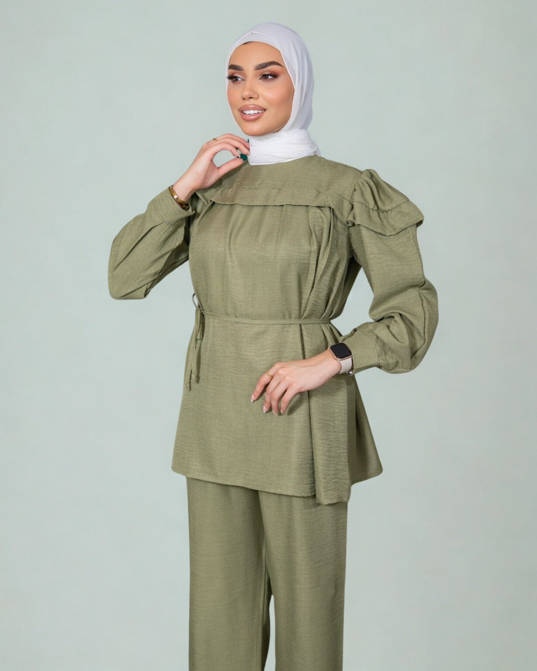 Woman wearing an olive green outfit with a matching hijab on a light gray background