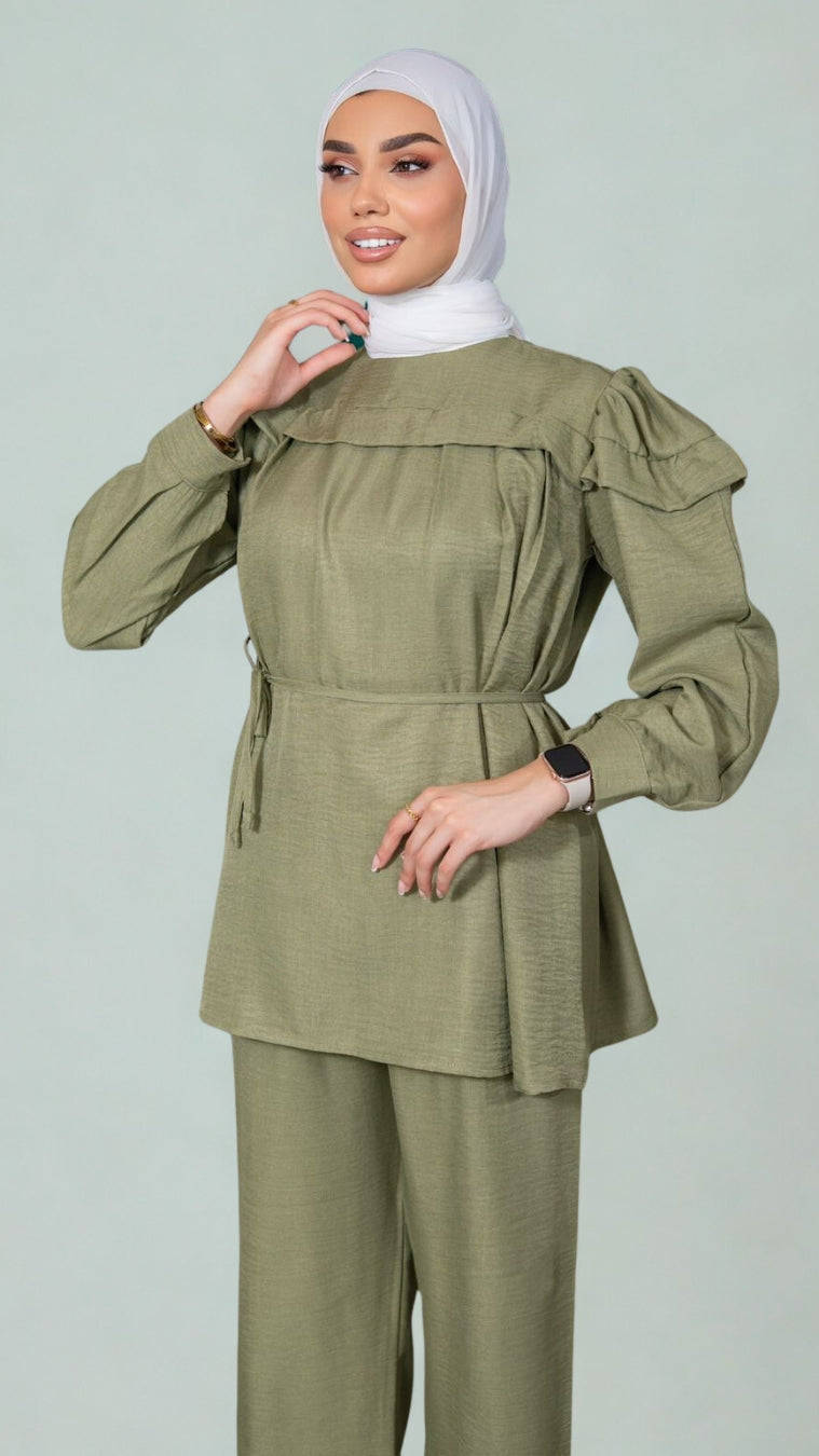 Woman wearing an olive green outfit with a matching hijab on a light gray background