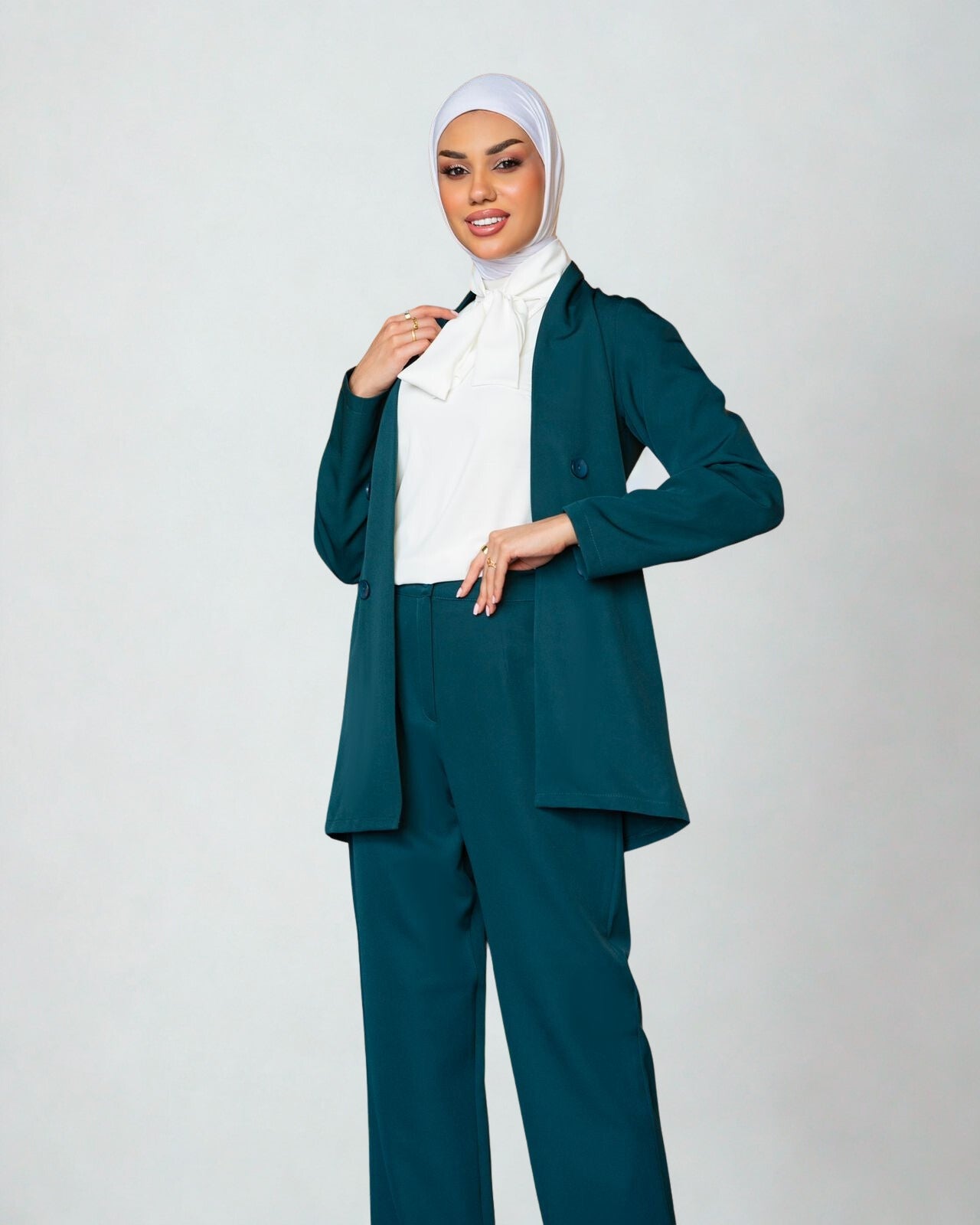 Woman wearing a teal suit with a white hijab on a plain background