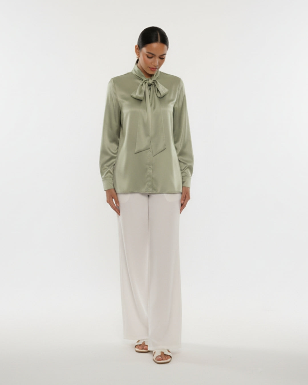 Woman wearing a green blouse with a bow tie and white pants on a white background