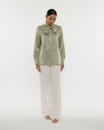 Woman wearing a green blouse with a bow tie and white pants on a white background