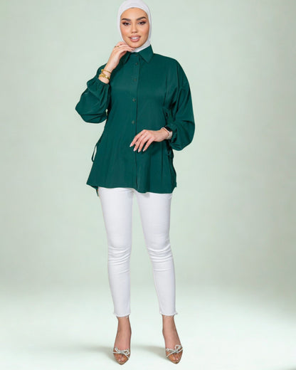 Woman wearing a green shirt and white pants on a light gray background