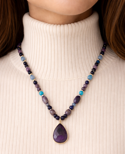 Necklace with a teardrop pendant worn by a person in a white turtleneck.