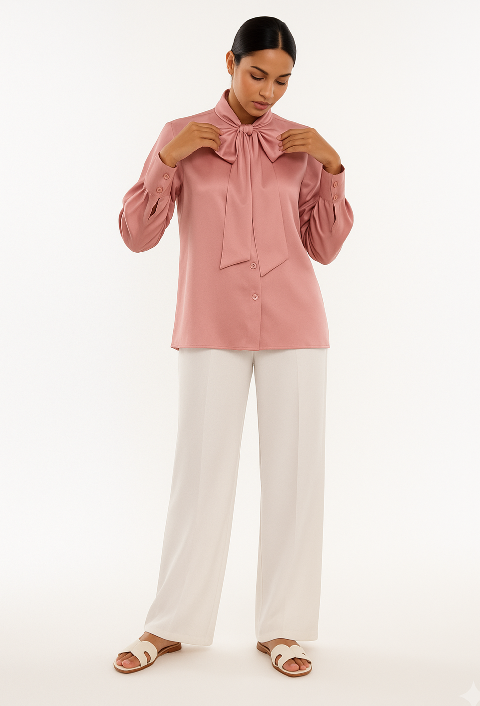 Woman wearing a pink blouse with a bow detail and white pants on a white background
