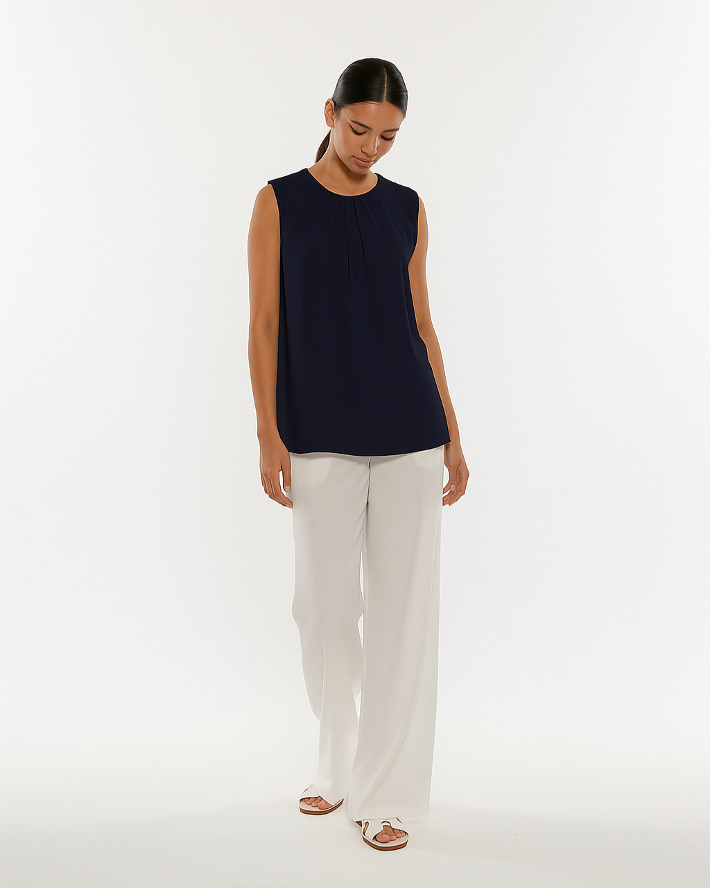 Woman wearing a navy sleeveless top and white pants on a white background