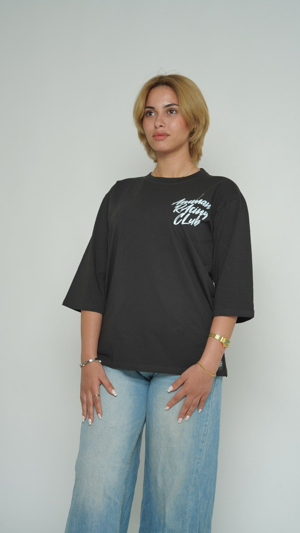 Person wearing a black t-shirt with white text and light blue jeans against a plain background
