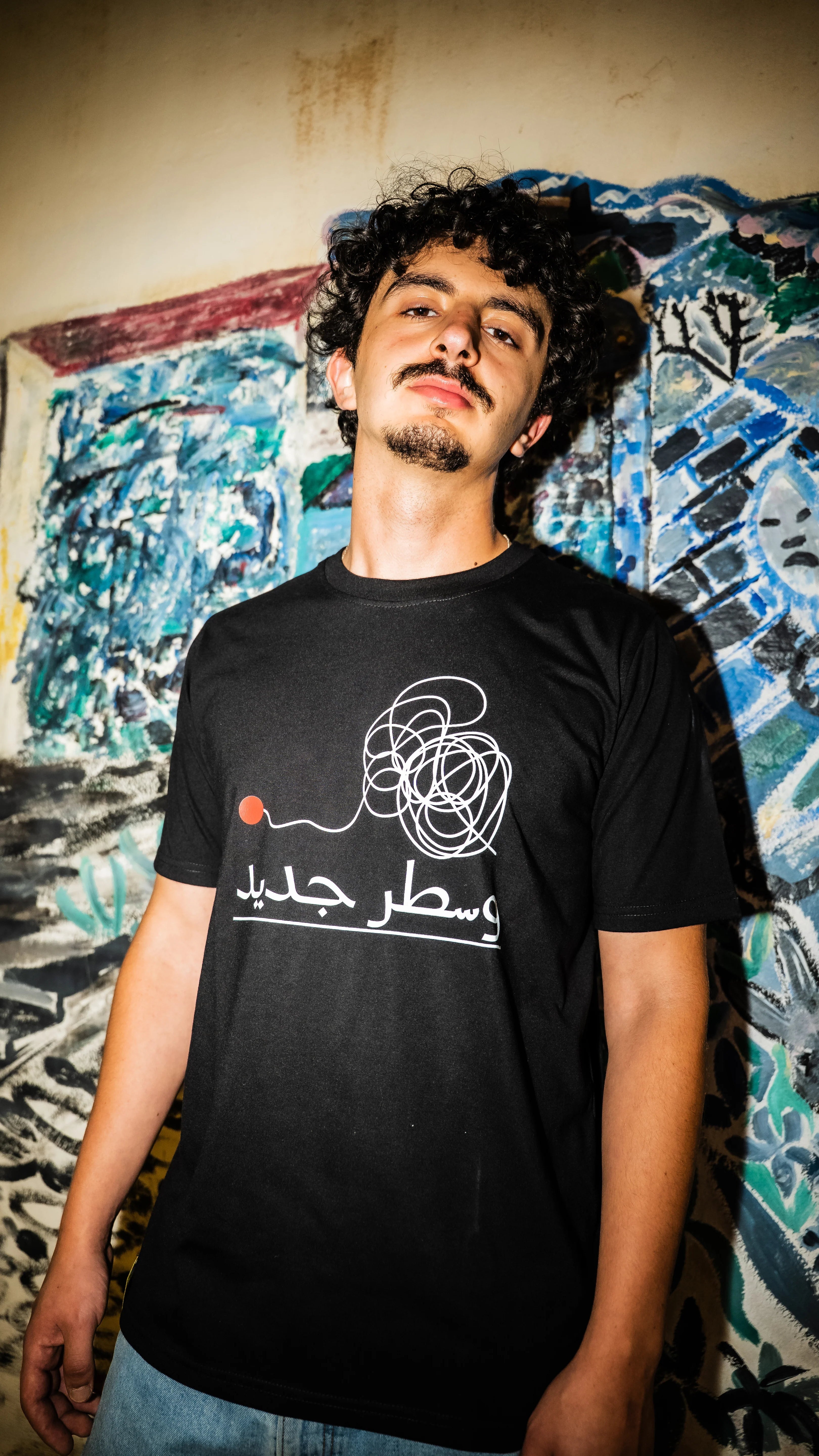 Man wearing a black t-shirt with white text and design against a colorful mural background