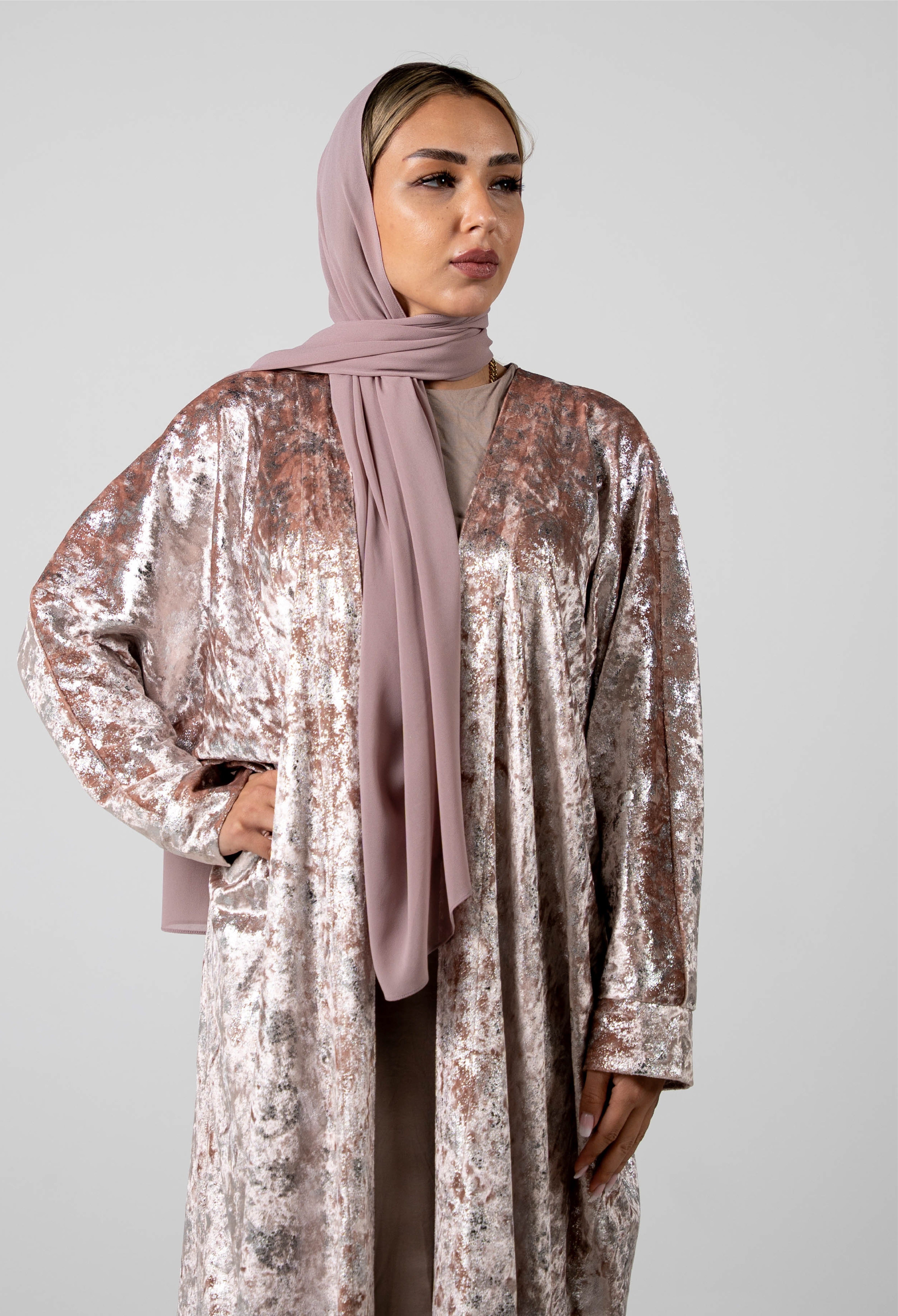 Woman wearing a sparkling silver outfit with a pink hijab against a plain background