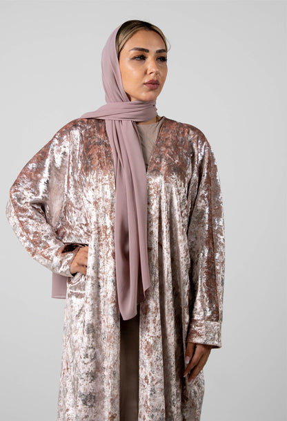 Woman wearing a sparkling silver outfit with a pink hijab against a plain background