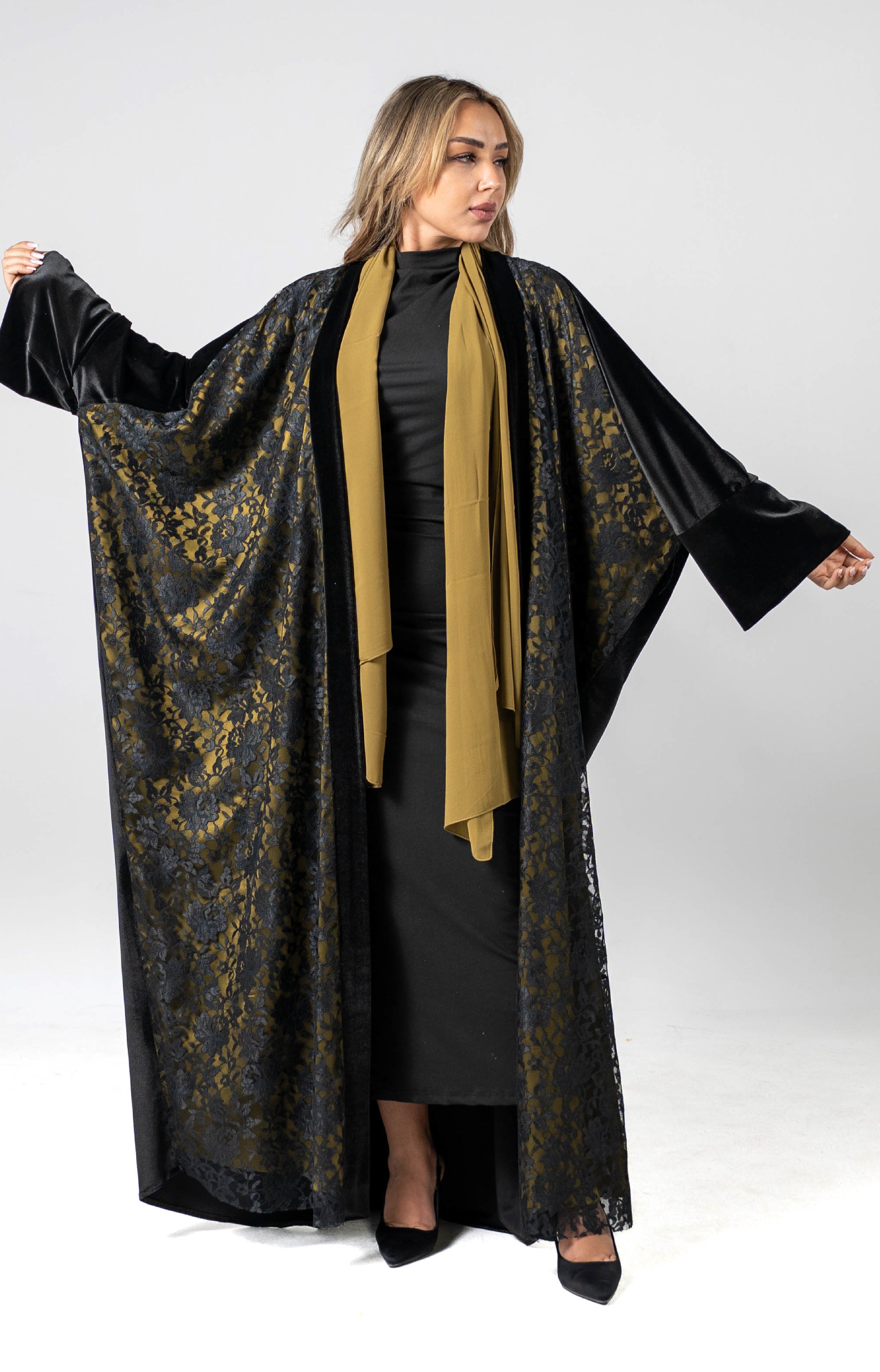 Woman wearing a black and gold abaya with a beige scarf on a white background