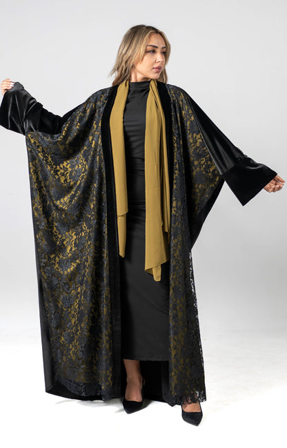 Woman wearing a black and gold abaya with a beige scarf on a white background