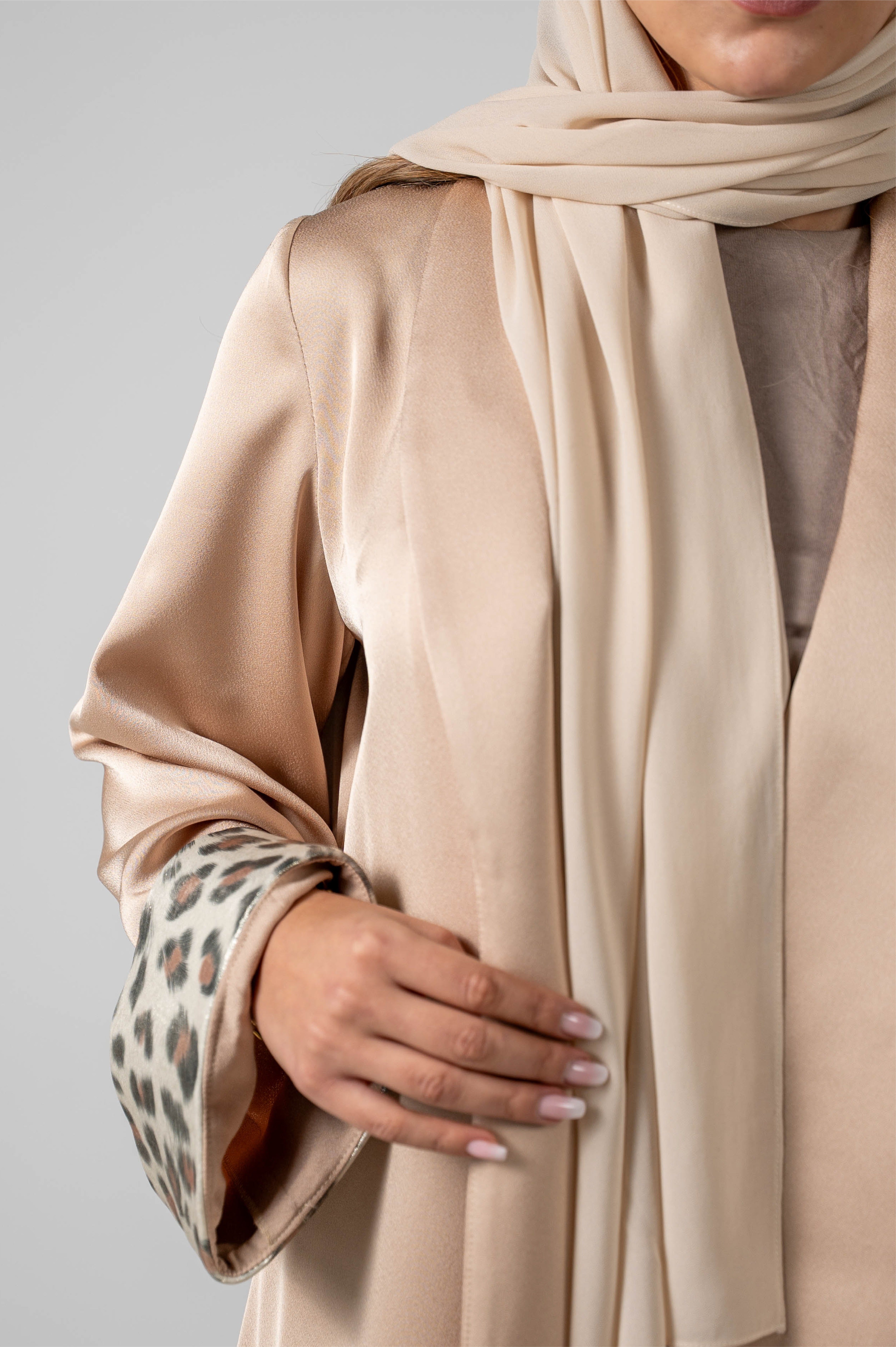 Person wearing a beige hijab and coat with a neutral background
