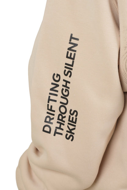 Beige hoodie with text 'Drifting Through Silent Skies' on a beige background