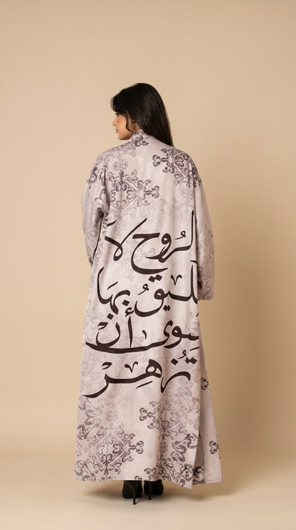 Woman wearing a long, light-colored coat with Arabic calligraphy on a beige background