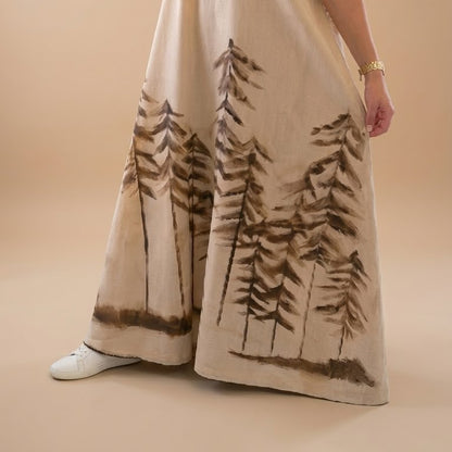 Long beige pants with tree pattern worn by a person on a beige background