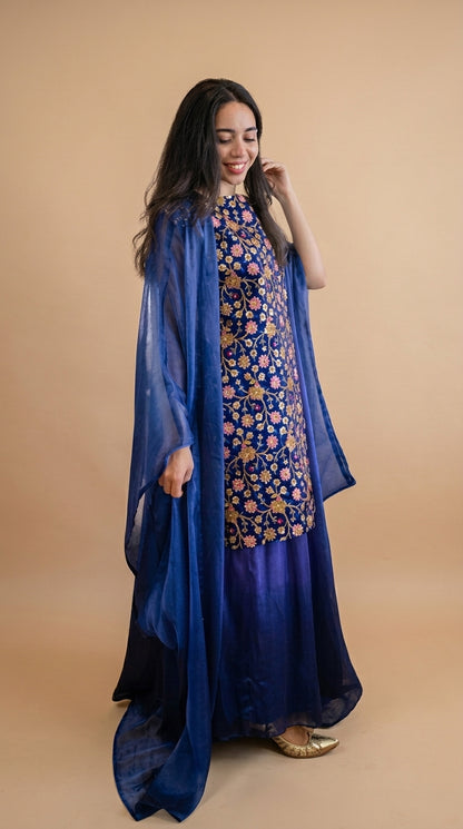 Woman wearing a blue floral dress with a matching dupatta on a beige background