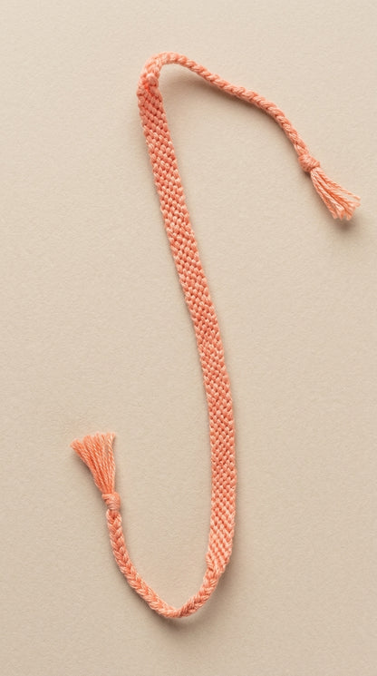 Braided coral-colored cord with tassels on a beige background
