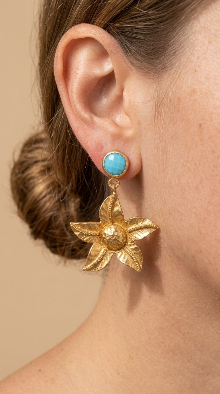 Gold star-shaped earring with turquoise stone worn by a person against a beige background
