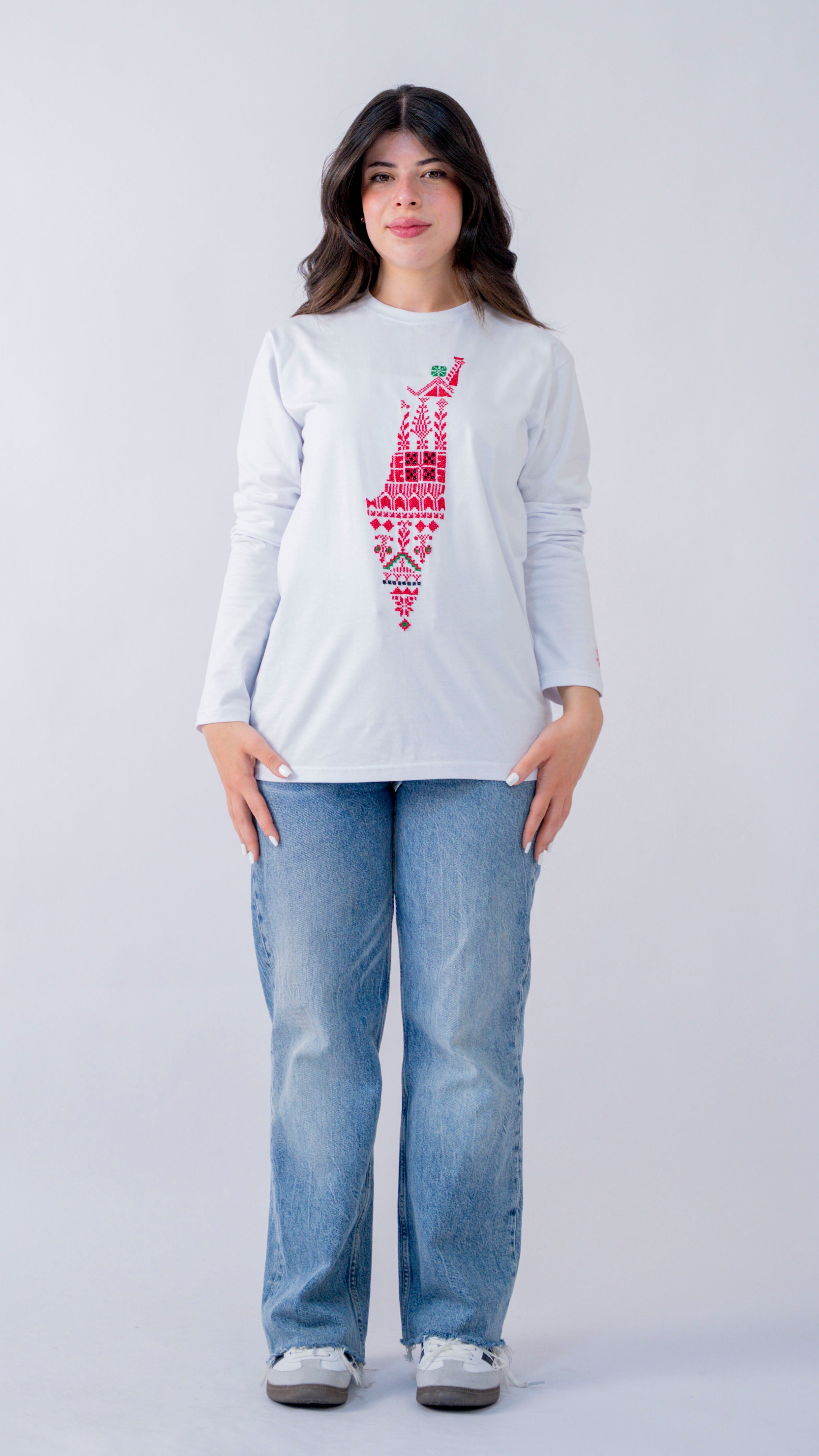 Person wearing a white long-sleeve shirt with a red graphic design and blue jeans on a white background