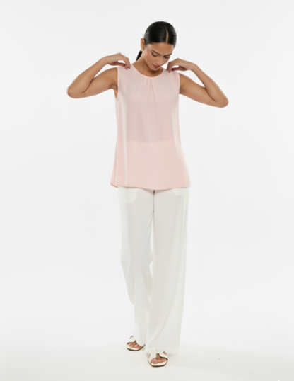 Woman wearing a light pink sleeveless top and white pants on a white background