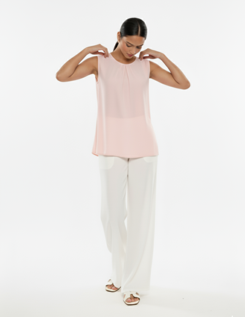 Woman wearing a light pink sleeveless top and white pants on a white background