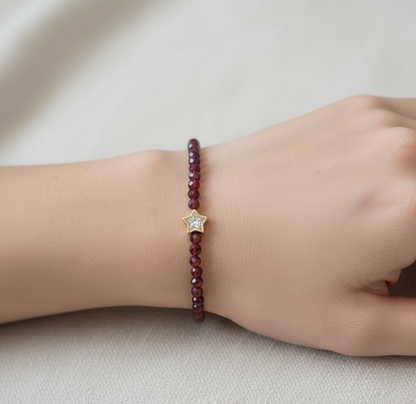 Burgundy beaded bracelet with a star charm on a wrist against a neutral background