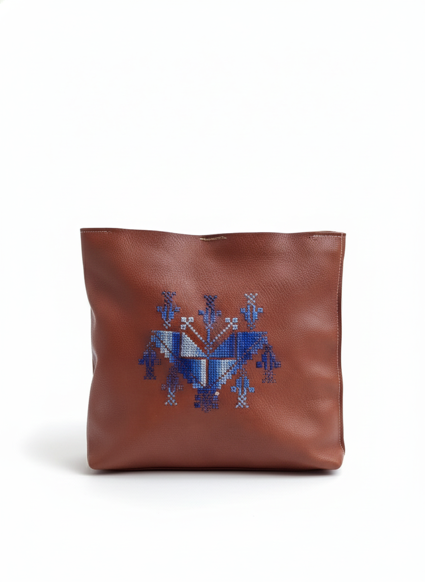 Brown leather bag with blue embroidered design on a white background