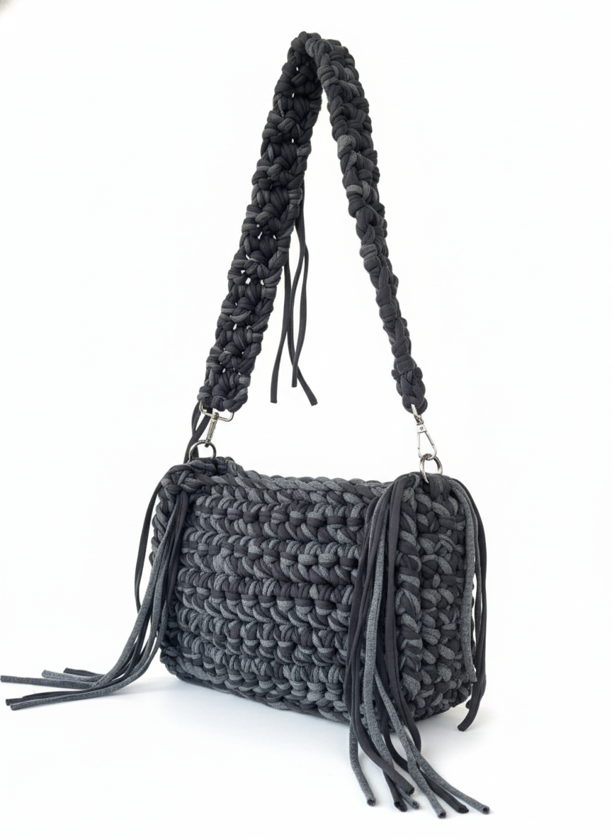 Black woven handbag with braided handle and fringes on a white background