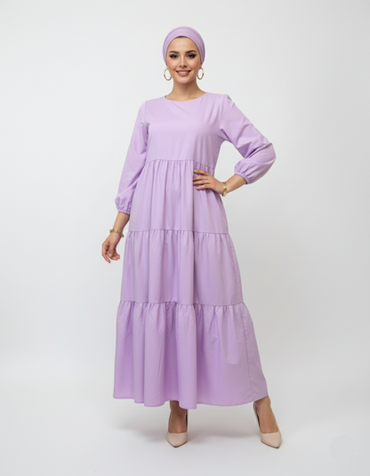 Woman wearing a long lilac dress with a matching headscarf on a white background