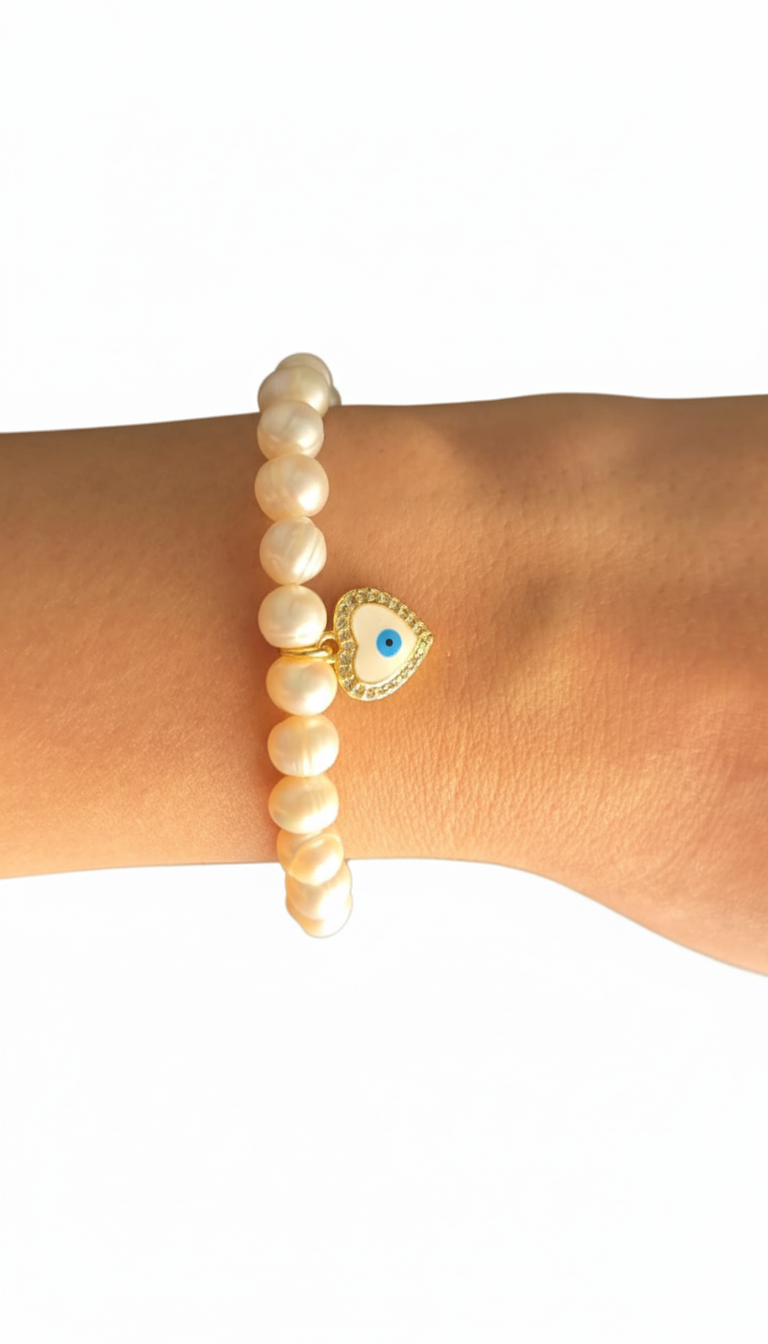 Pearl bracelet with a gold evil eye charm on a wrist against a white background