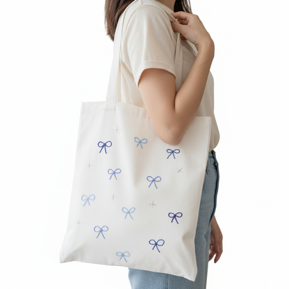 Person holding a white tote bag with blue bow patterns against a white background