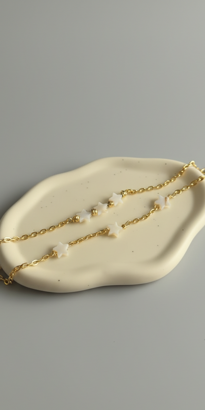 Gold chain necklace with small pearls on a beige dish against a gray background