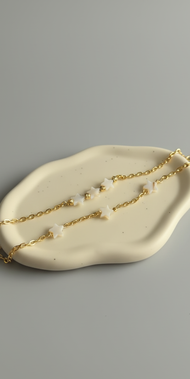 Gold chain necklace with small pearls on a beige dish against a gray background