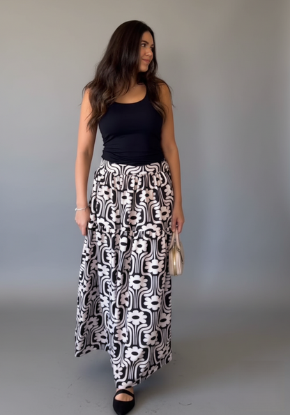 Woman wearing a black top and patterned skirt against a plain background