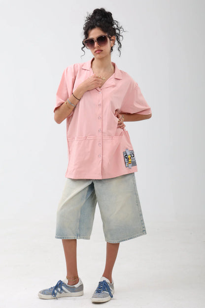 Person wearing a pink shirt with patches and light blue shorts on a white background