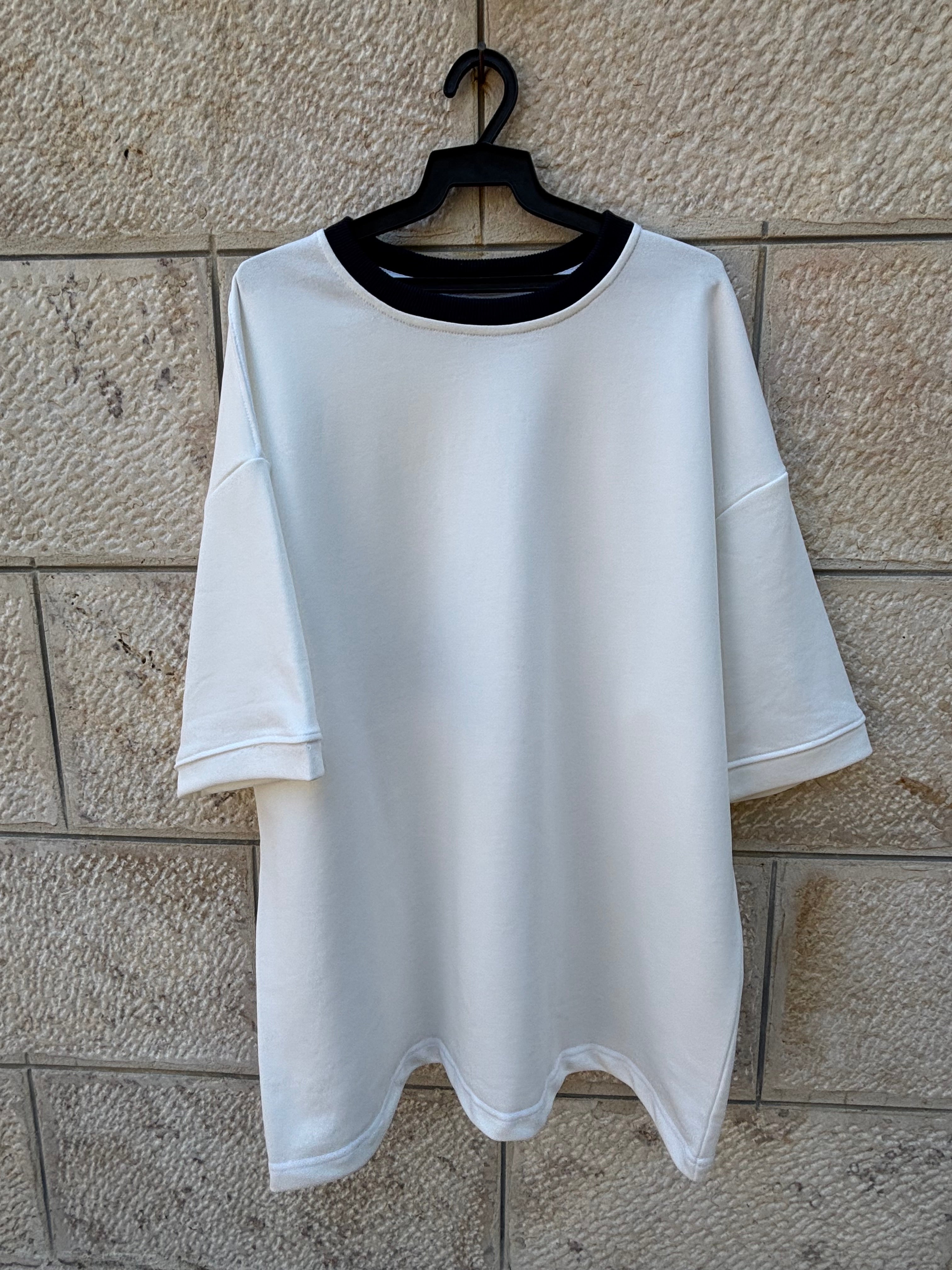 A white short-sleeve t-shirt with a scalloped hem and a black collar, laid flat on a light beige stone-tile floor.
