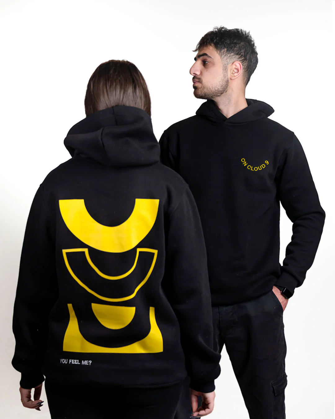 Two people wearing black hoodies with yellow designs on a white background