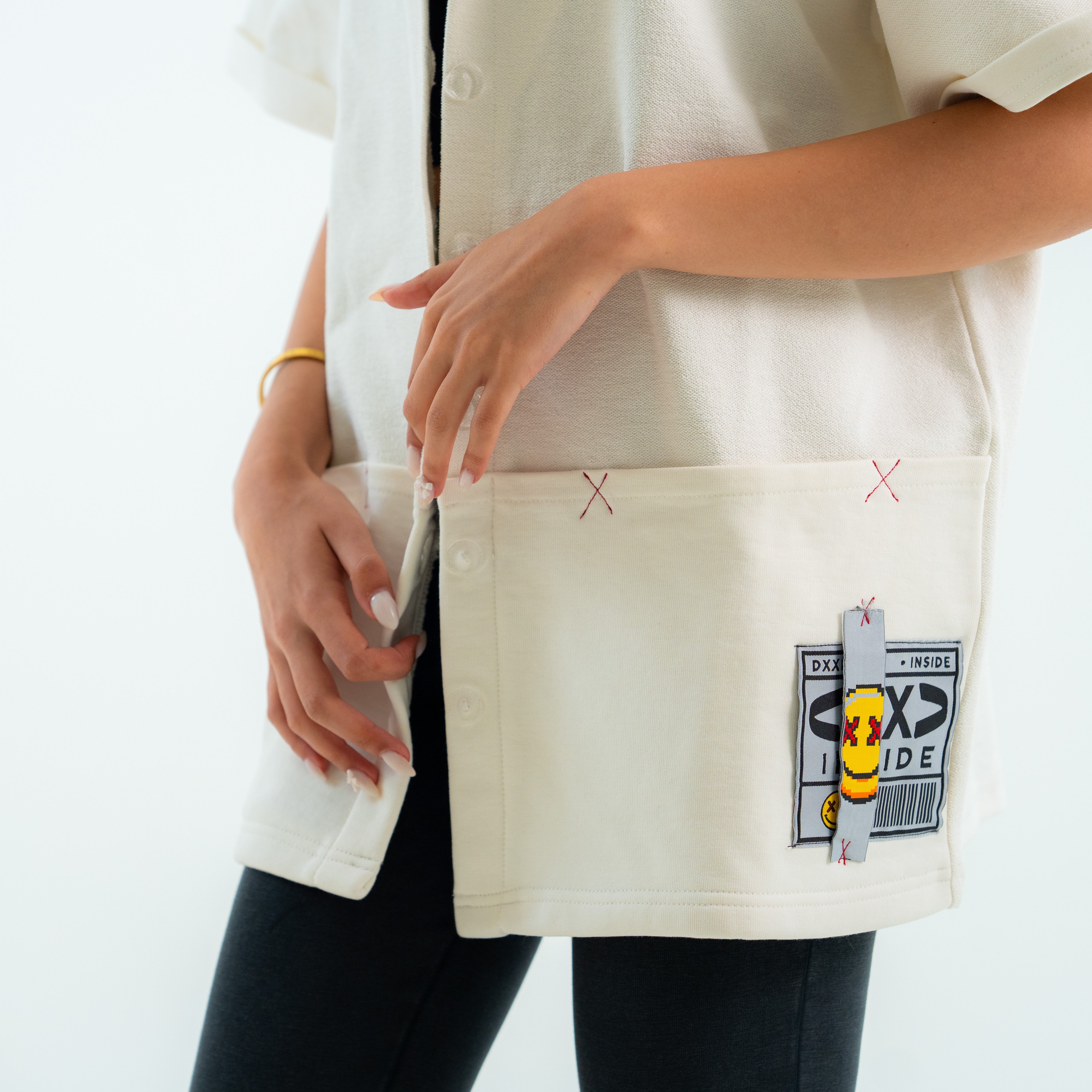 Person wearing a white shirt with a unique design on the pocket against a plain background