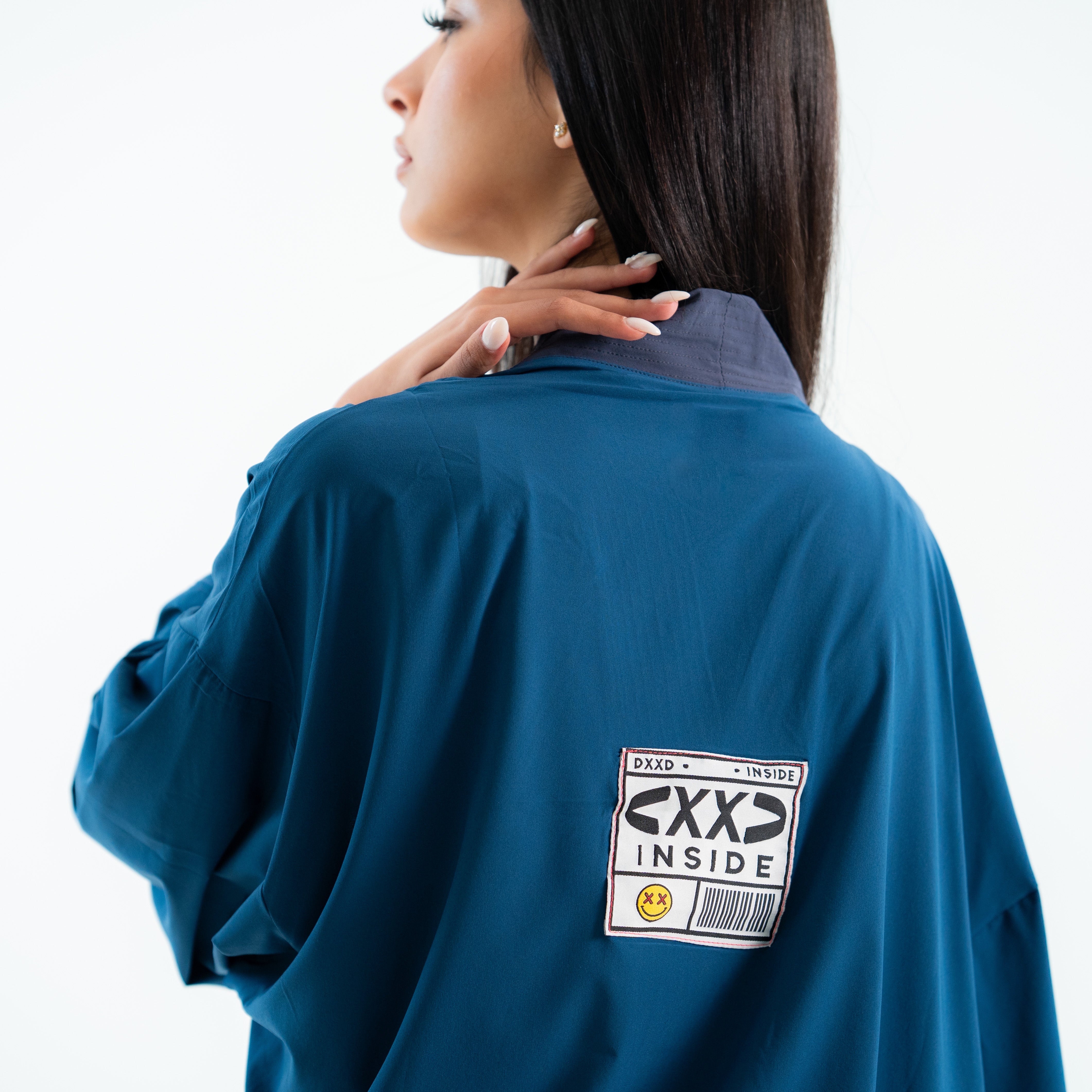 Woman wearing a blue jacket with a 'XXD Inside' patch on the back against a white background