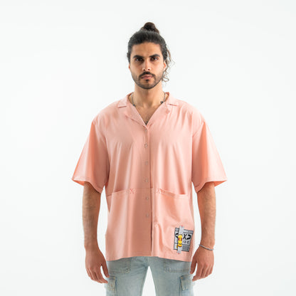 Man wearing a light pink button-up shirt with a patch on a white background