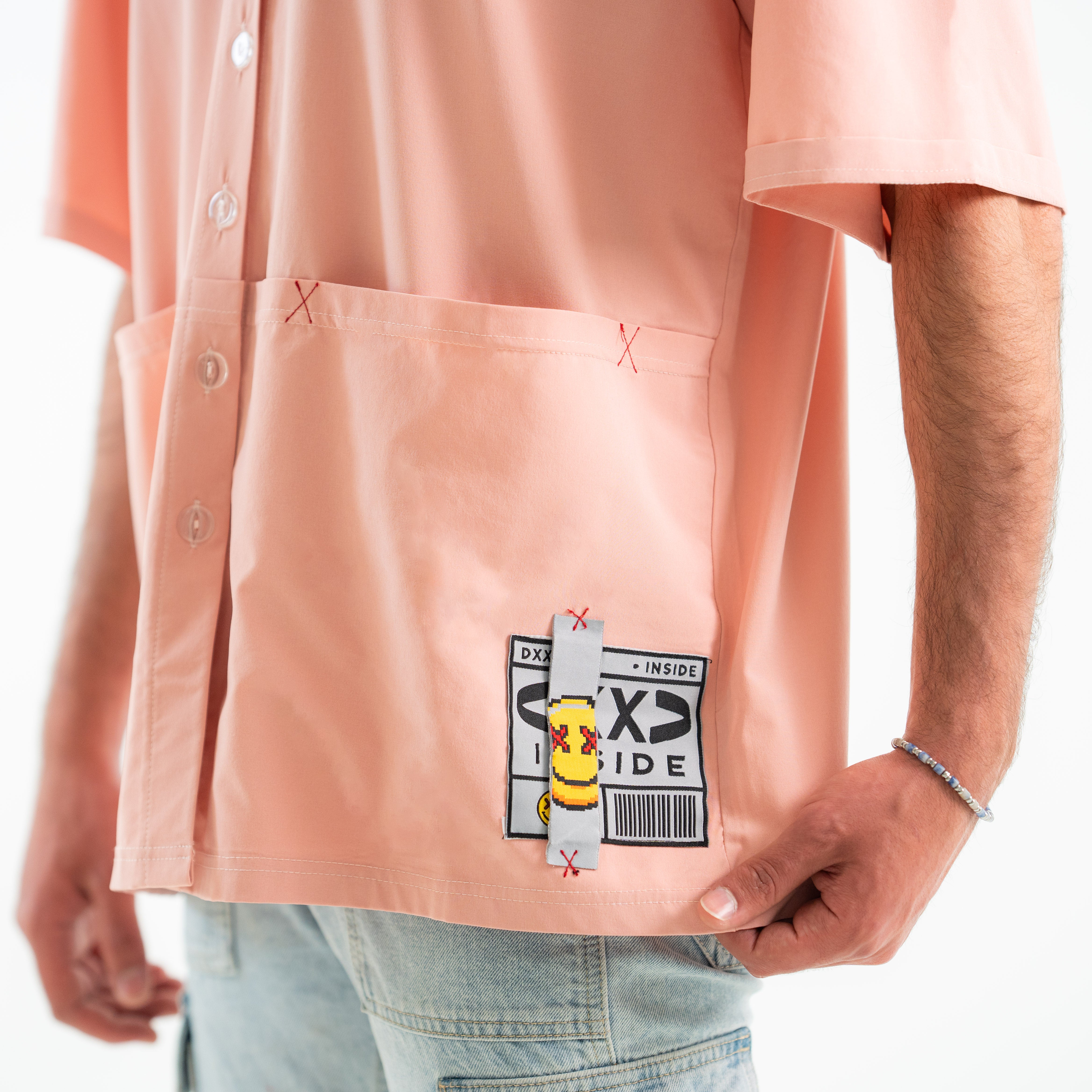 Person wearing a light pink shirt with a graphic design on the chest pocket against a white background