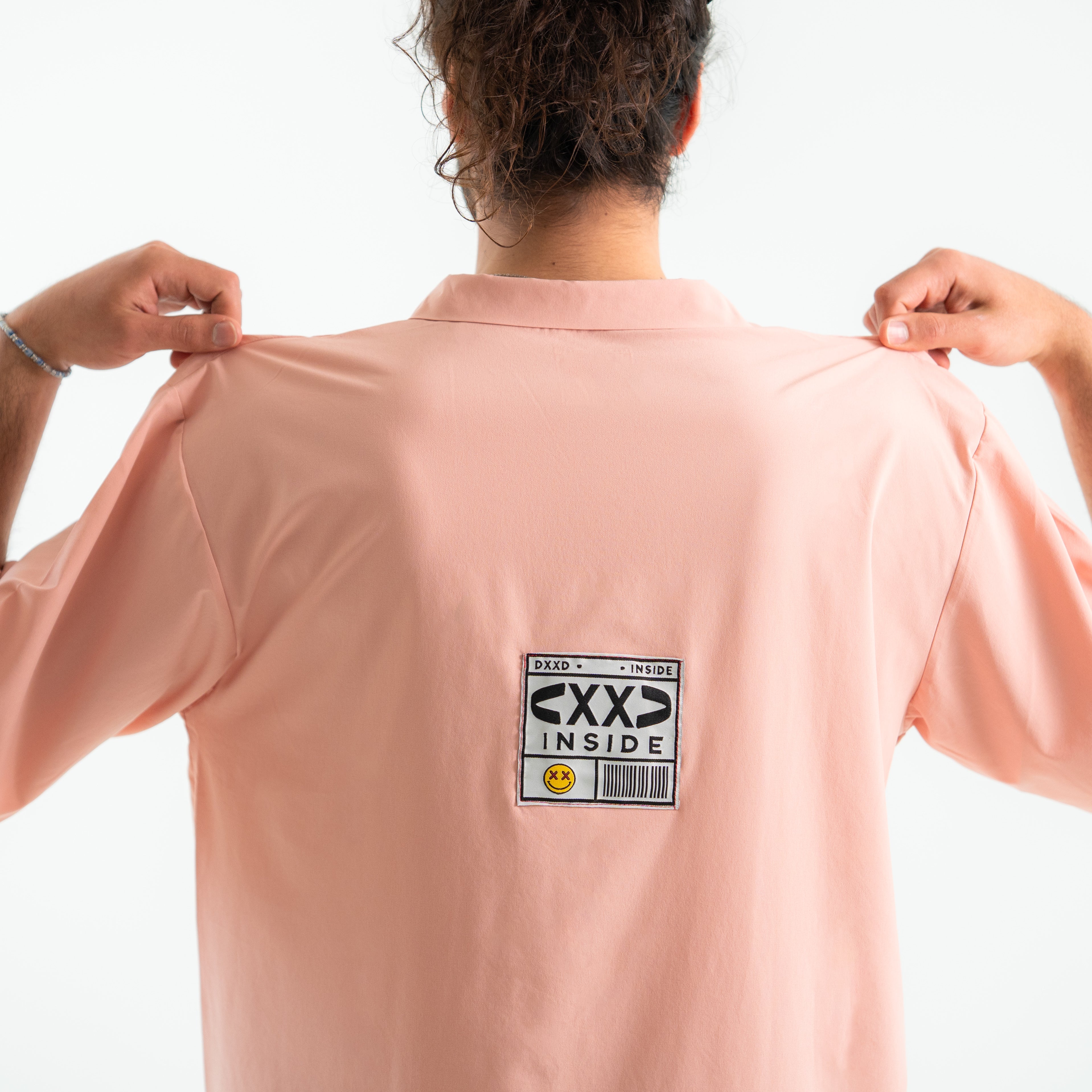 Person wearing a light pink shirt with a label on the back against a white background