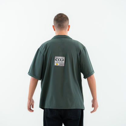 Man wearing a green polo shirt with a logo on the back against a white background