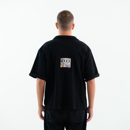 Person wearing a black polo shirt with a logo on the back against a white background