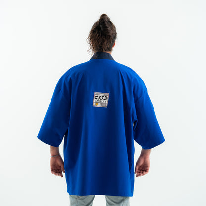 Person wearing a blue martial arts uniform with a visible brand logo on the back against a white background