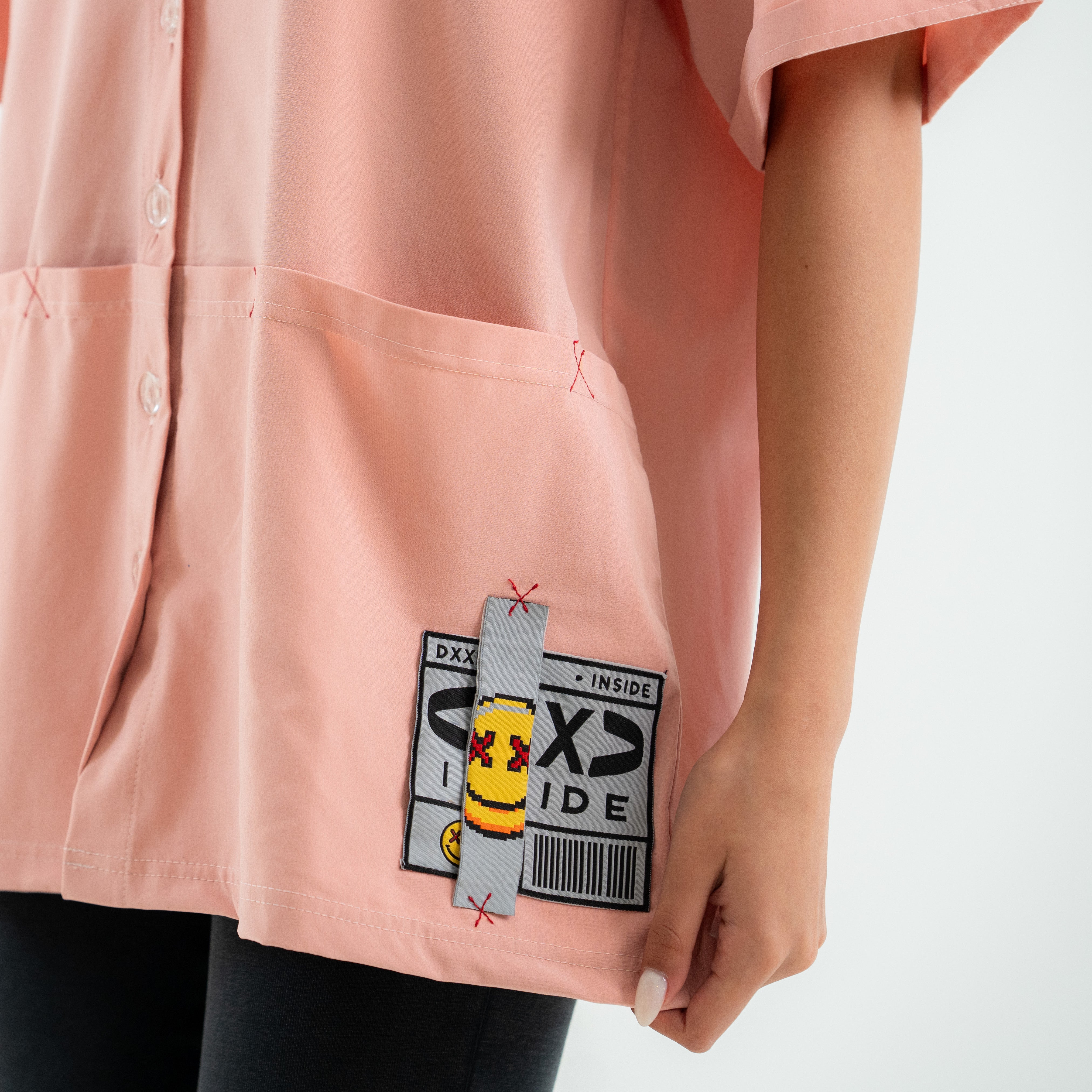 Pink shirt with a cartoon character patch on the pocket against a white background