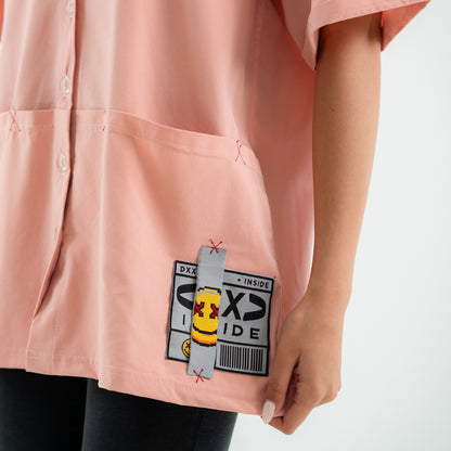 Pink shirt with a cartoon character patch on the pocket against a white background