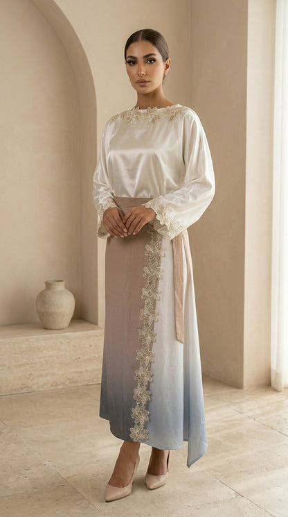 Woman wearing a long, light-colored dress with lace details in a softly lit room.